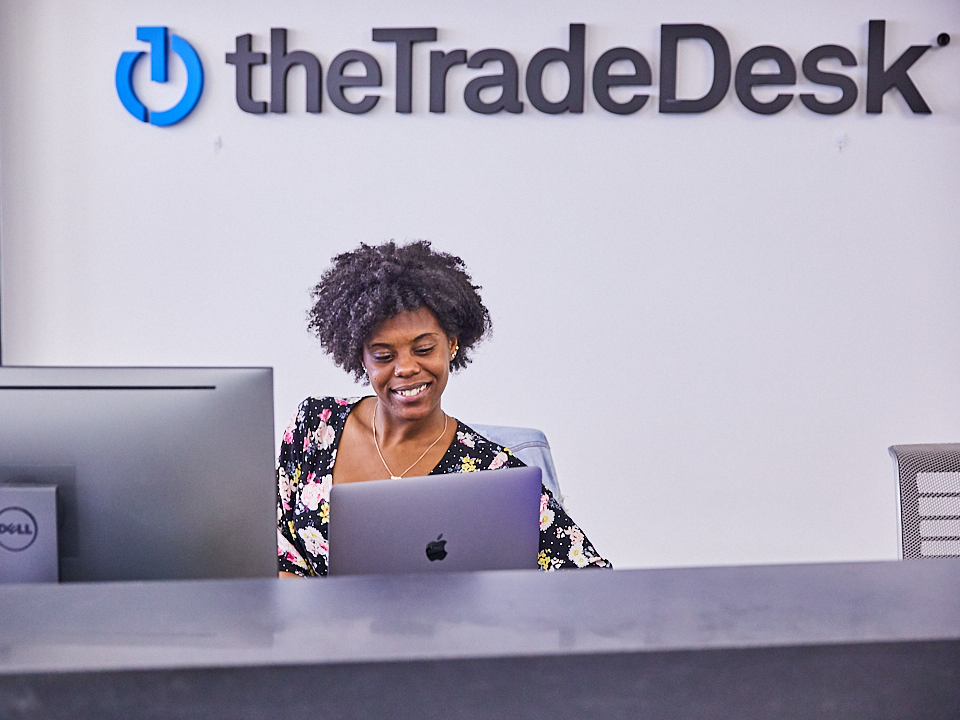 A woman sits at the reception desk with The Trade Desk logo overhead 