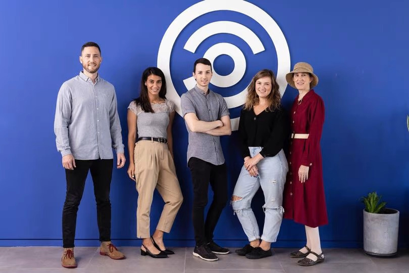 Carbyne team members standing in front of a blue wall with the company logo on it