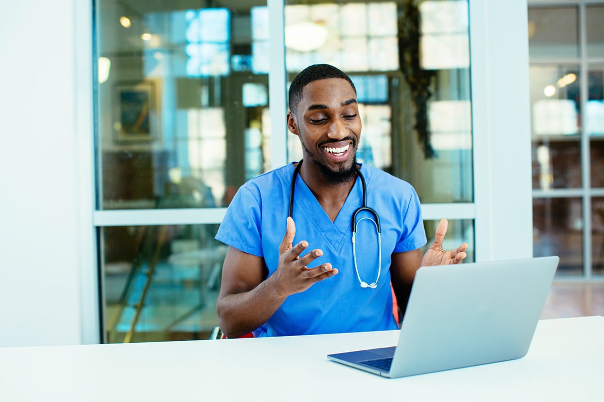 male doctor wearing blue scrubs uniform using laptop to talk to patient online