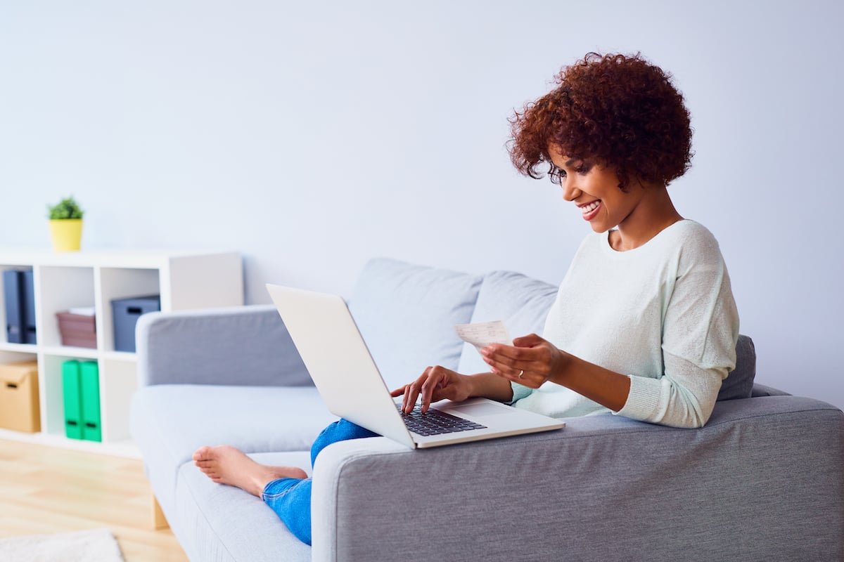 A woman sits on her couch with her credit card and laptop