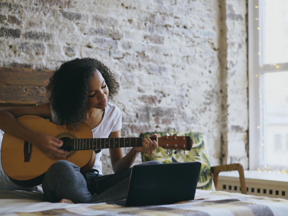 Young woman playing guitar with her laptop open