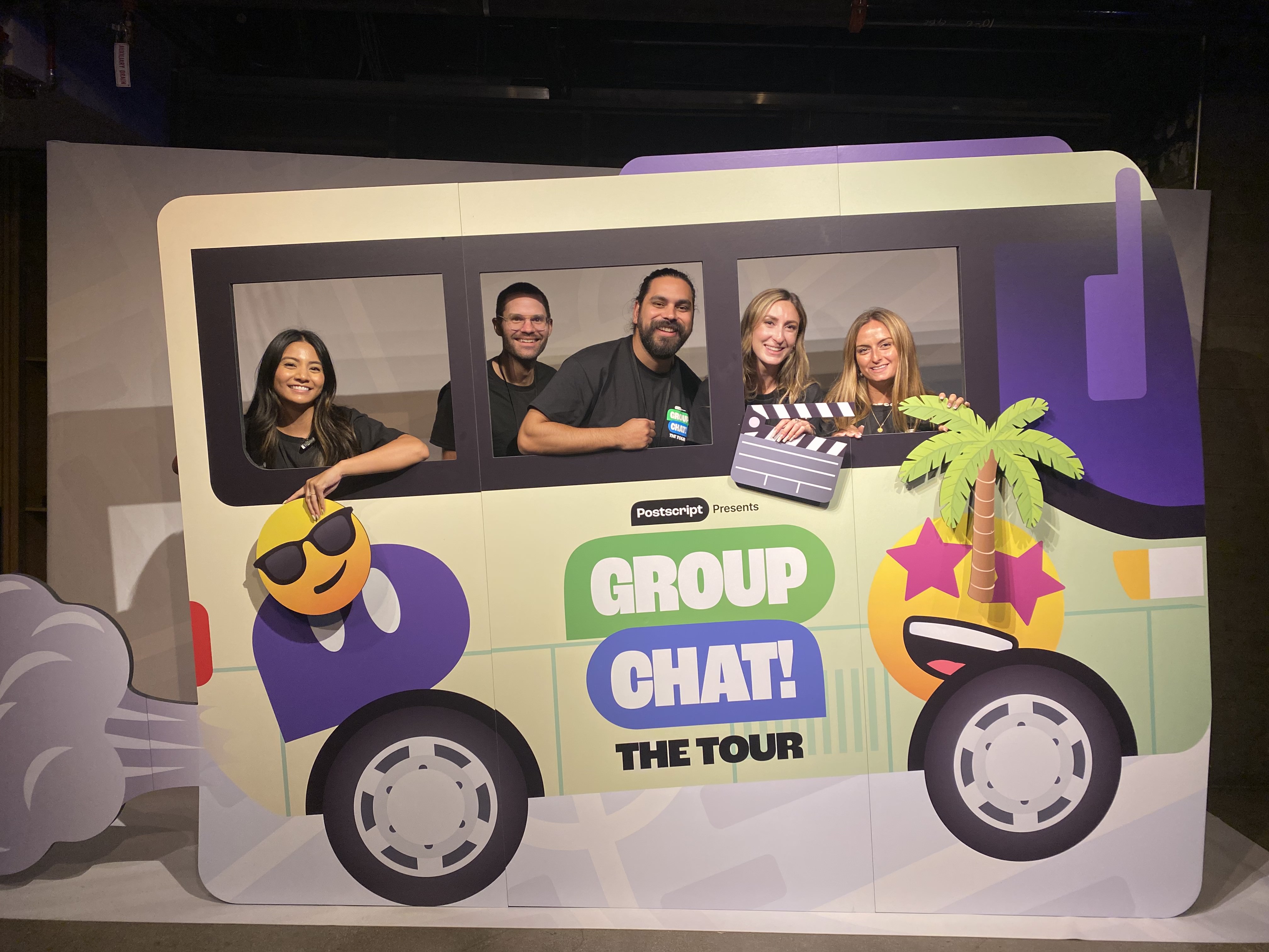 Five of Postscript's employees posing in a cardboard cartoon bus that reads "Group Chat! The Tour"