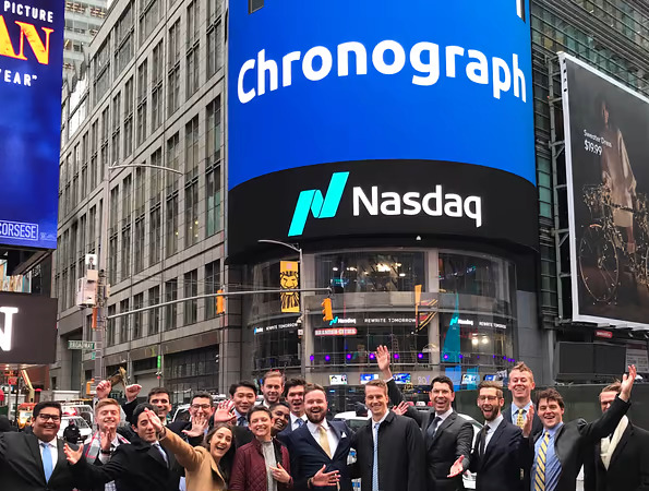 A group of Chronograph employees pose in front of a Nasdaq billboard.