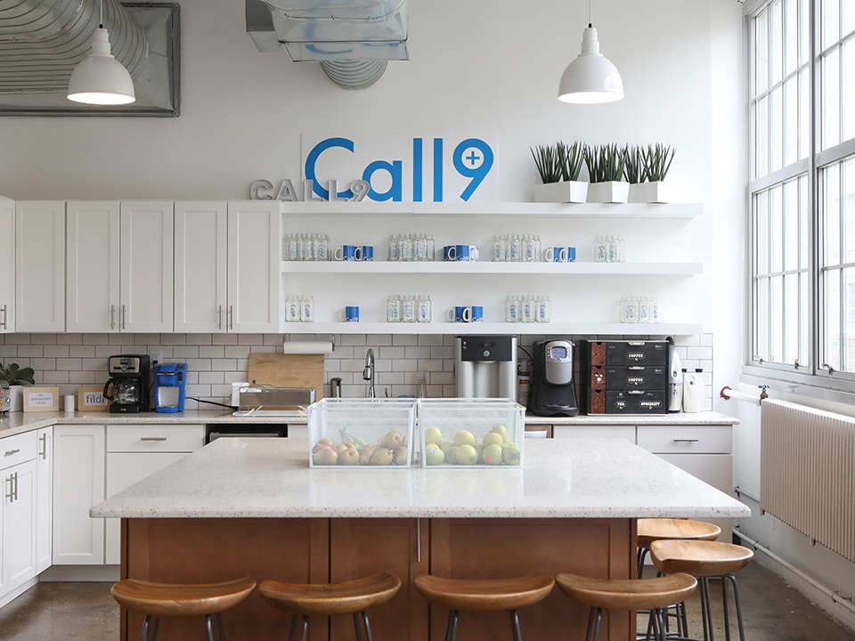 A bright kitchen counter sits in the middle of a Kitchen with the large Call9 logo over its countertops. 