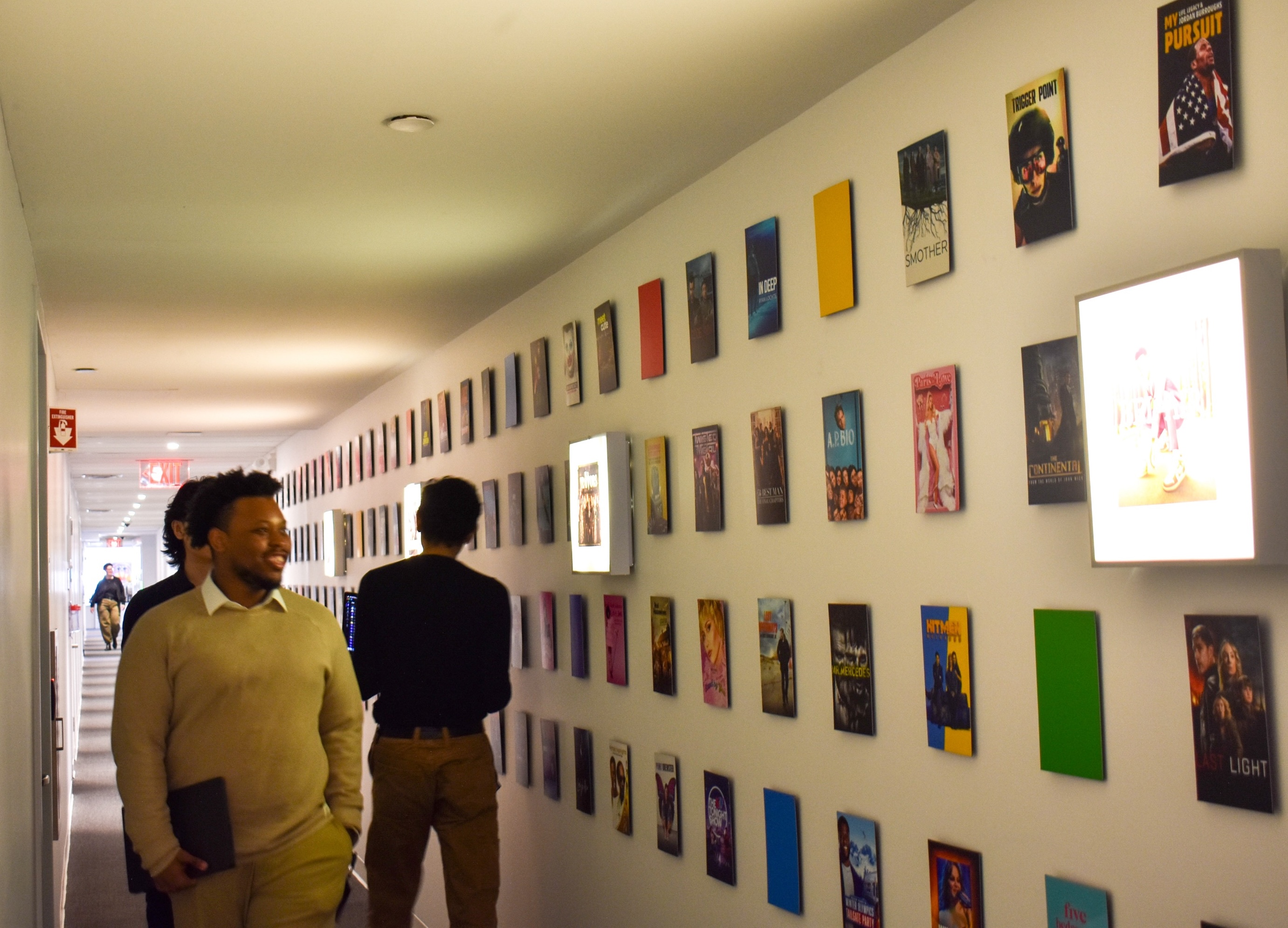 NBCUniversal team members walk through office hallway lined with artwork promoting the brand’s TV series. 