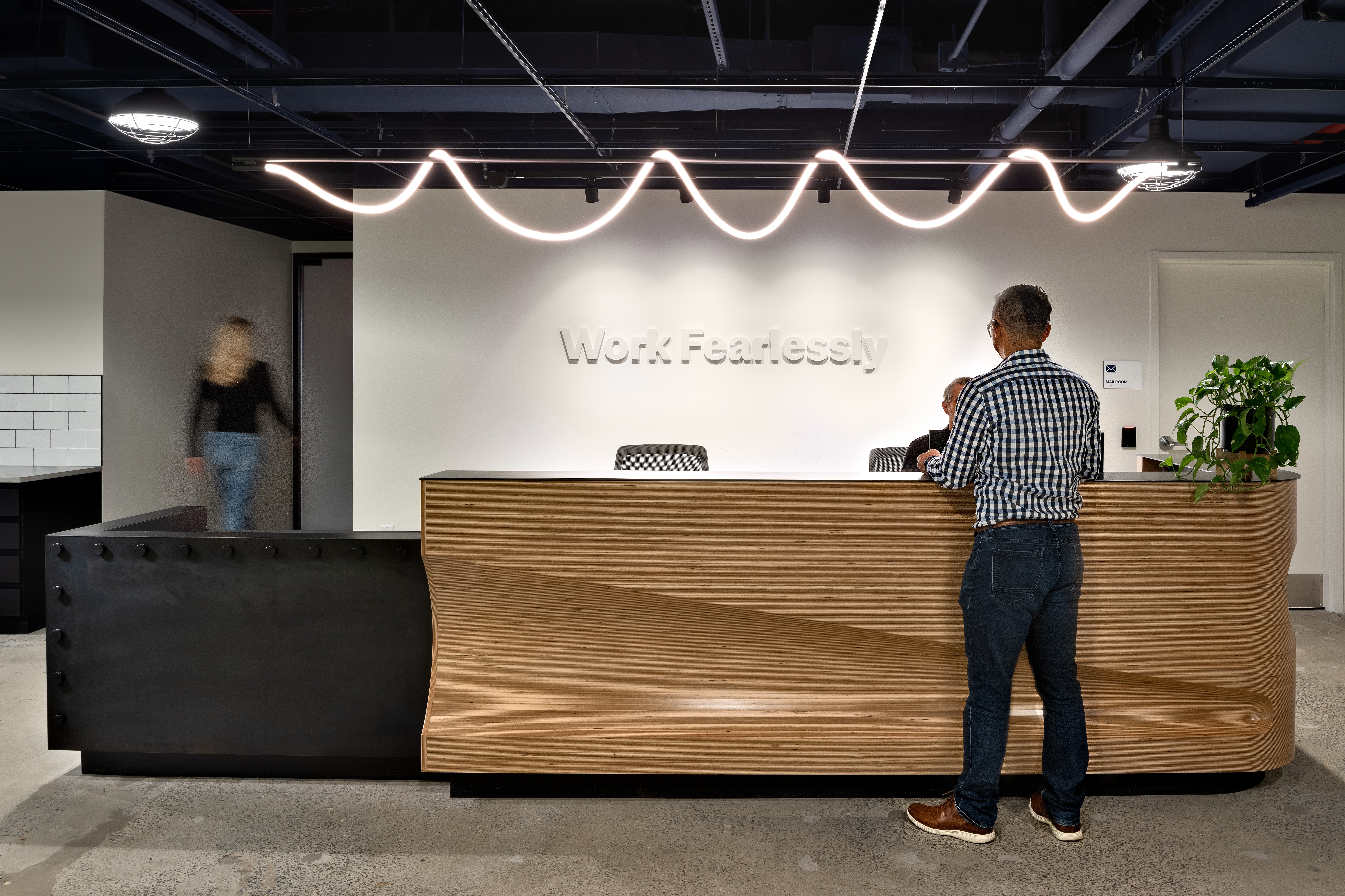 Photo of Justworks’ reception desk with “Work Fearlessly” on wall and zigzag lighting above.