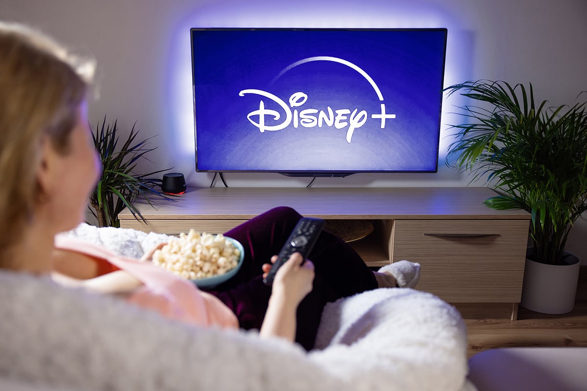 Woman watching TV at home with Disney+ logo on the screen.