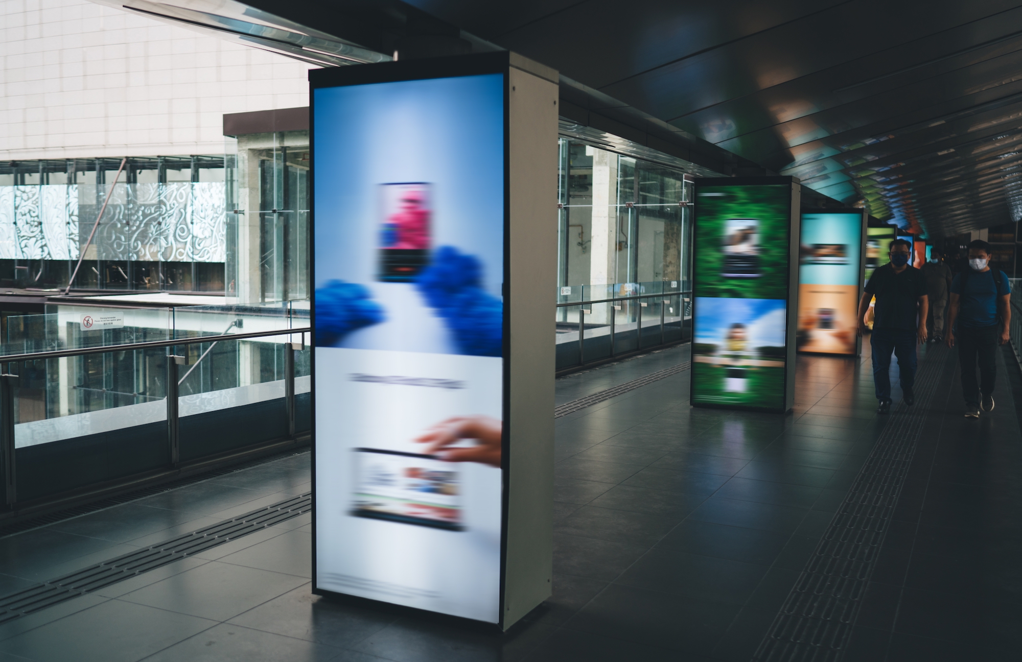 Blurred digital ads in a public walkway are pictured.