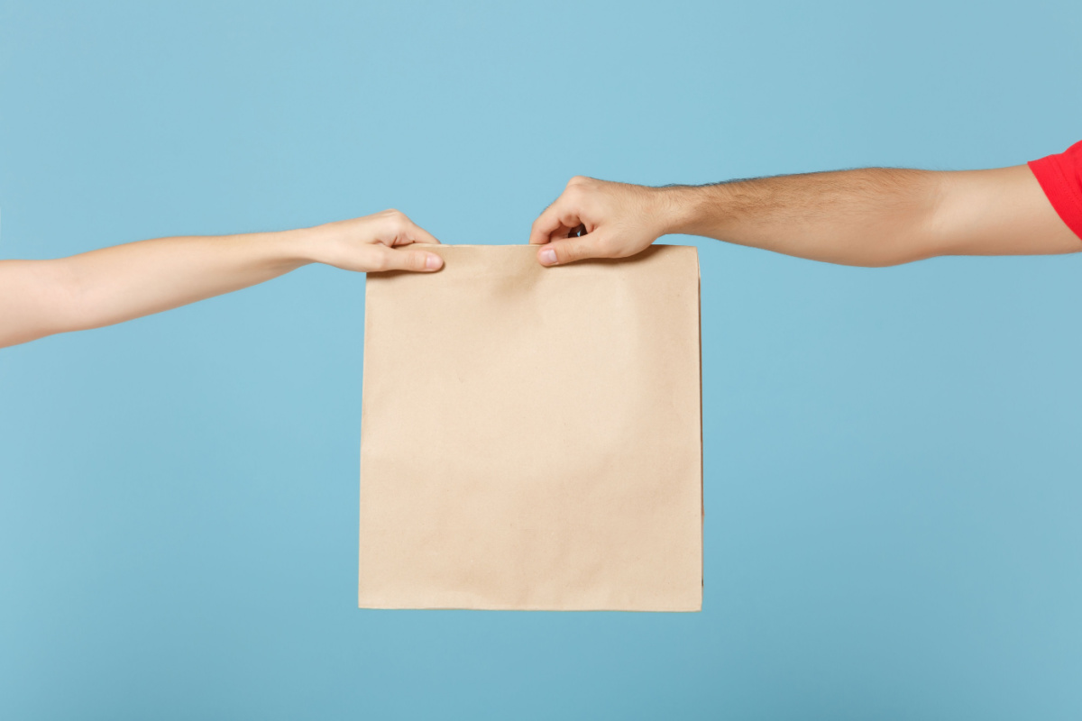 A delivery person handing a paper bag to a customer set against a blue background. 