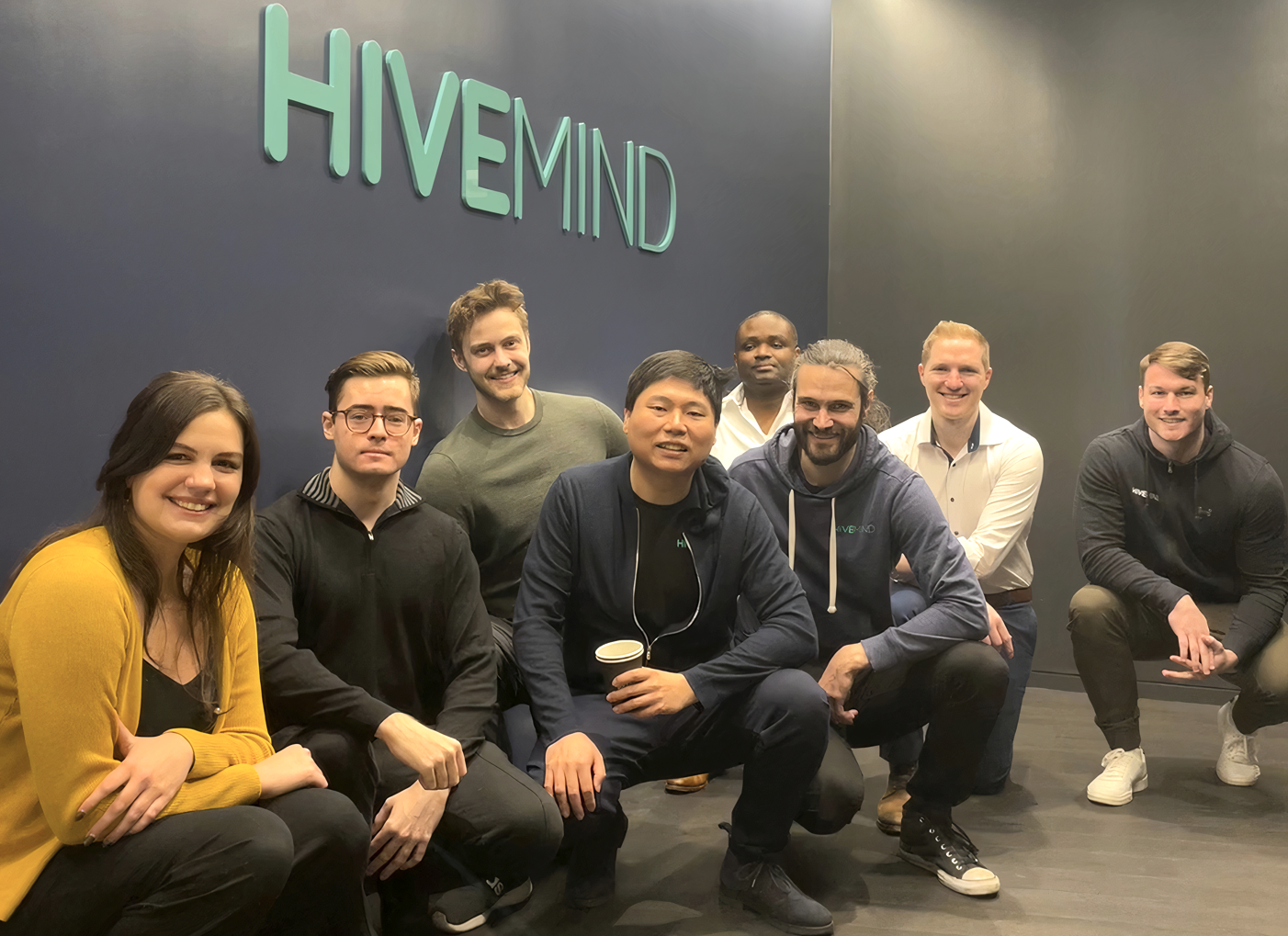 The Hivemind team poses in front of their logo on the wall of their new NYC headquarters.