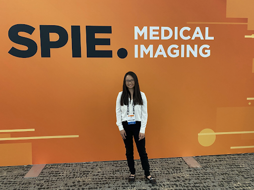 Merck team member stands in front of orange wall with branding reading "SPIE Medical Imaging"