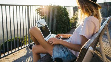 Image of a woman sitting out on a balcony doing work on a laptop as the sun sets