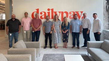 DailyPay team members in the office with the company logo on the wall behind them