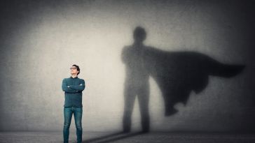 A man stands with a superhero's silhouette displayed behind him.