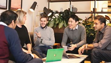 Chronosphere co-founded by CTO Rob Skillington and CEO Martin Mao gather around a table in the office with other employees.