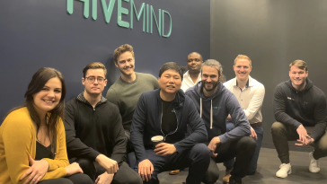 The Hivemind team poses in front of their logo on the wall of their new NYC headquarters.