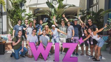 The Wiz team is pictured around a pink sculpture of the company logo.