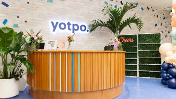 Photo of Yotpo’s front desk surrounded by plants with lighted logo sign on the wall behind